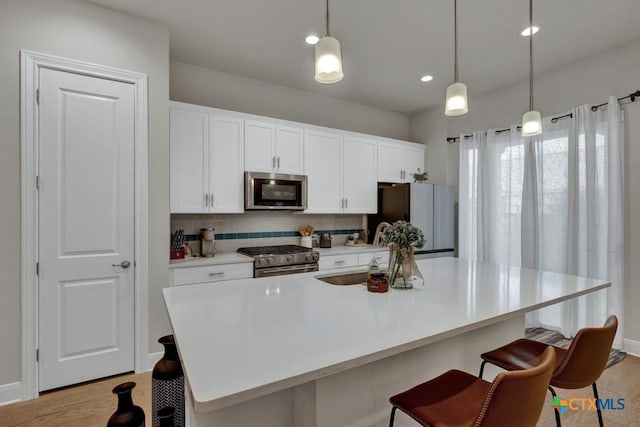kitchen with white cabinets, appliances with stainless steel finishes, light wood-style floors, a breakfast bar area, and tasteful backsplash