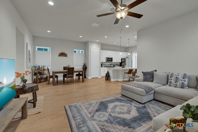 living room featuring a ceiling fan, visible vents, recessed lighting, and light wood finished floors