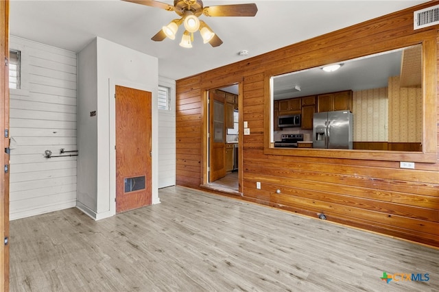 571 N Houston Ave, New Braunfels, TX 78130 - kitchen with stainless steel appliances, wood walls, light wood-type flooring, a ceiling fan, and brown cabinetry