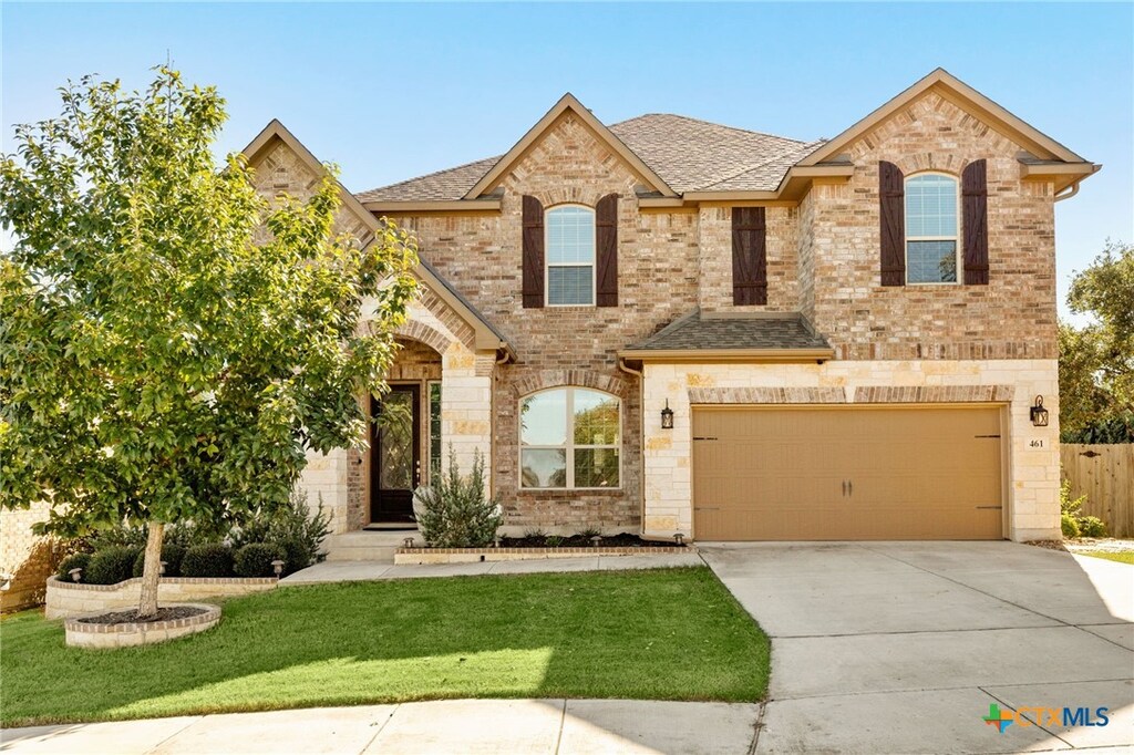 french country home featuring concrete driveway, fence, an attached garage, a front lawn, and brick siding