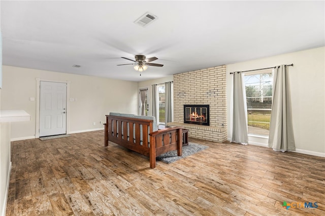 bedroom with baseboards, visible vents, a ceiling fan, hardwood / wood-style flooring, and a brick fireplace