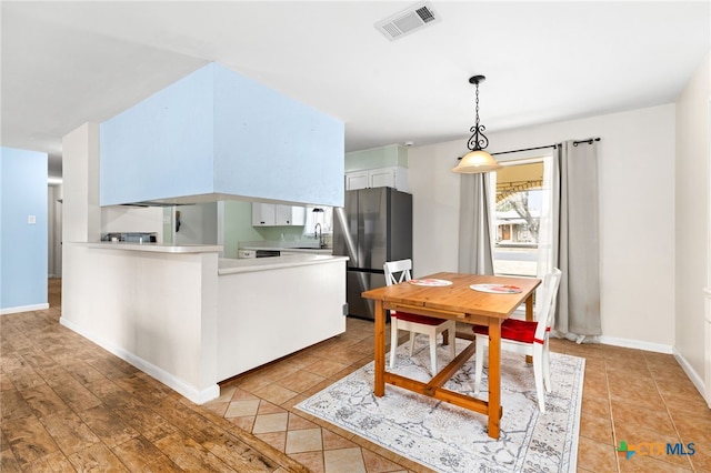 kitchen featuring visible vents, a peninsula, freestanding refrigerator, and baseboards