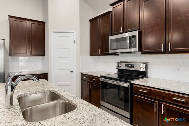 kitchen featuring decorative backsplash, appliances with stainless steel finishes, light stone countertops, dark brown cabinets, and sink