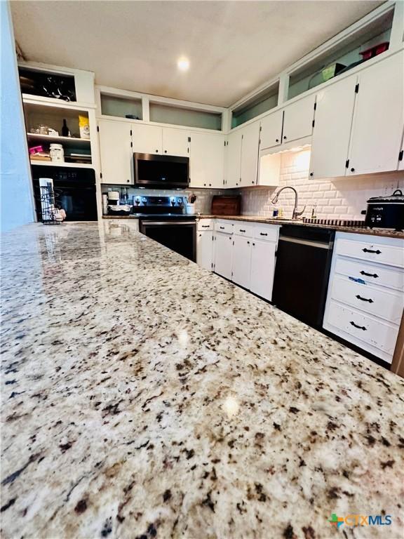 3043 Boys Ranch Rd, Kempner, TX 76539 - kitchen with black appliances, light stone countertops, white cabinets, and decorative backsplash
