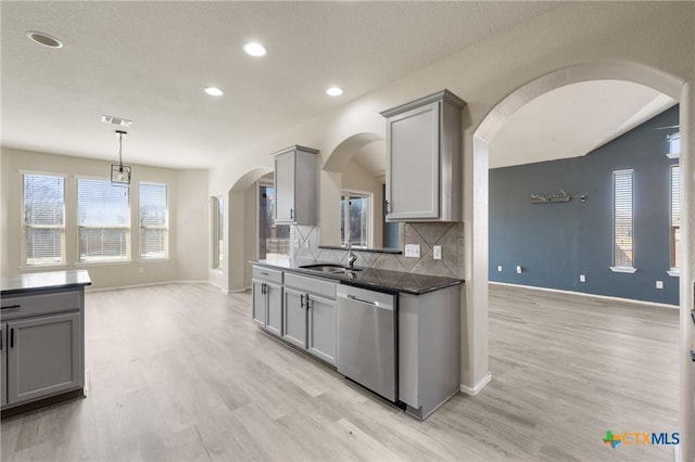 kitchen with arched walkways, stainless steel dishwasher, a sink, and gray cabinetry