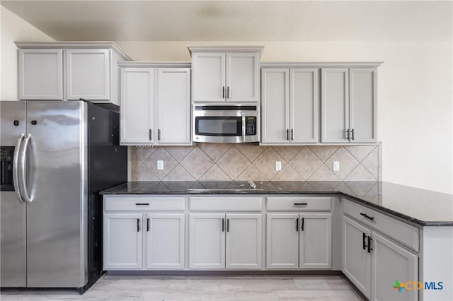 kitchen featuring light wood finished floors, appliances with stainless steel finishes, dark stone countertops, and backsplash