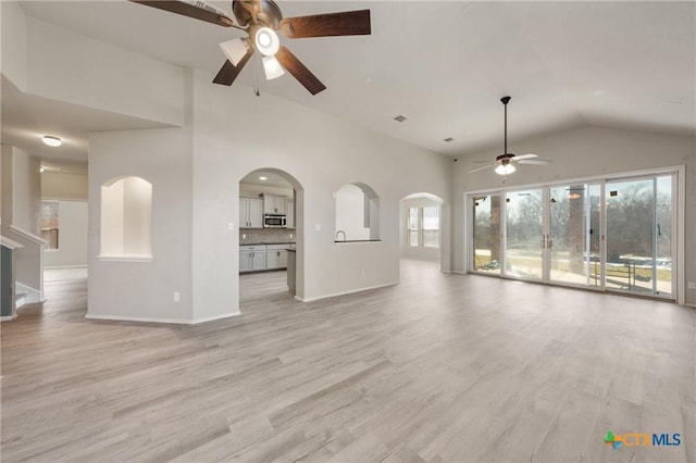 unfurnished living room with light wood-type flooring, ceiling fan, baseboards, and arched walkways