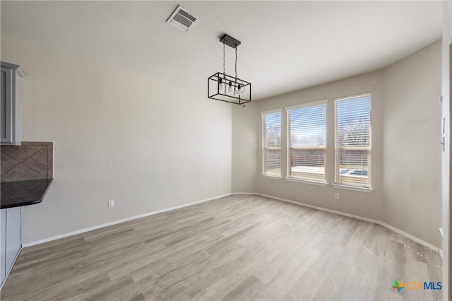 unfurnished dining area featuring an inviting chandelier, light wood-type flooring, visible vents, and baseboards