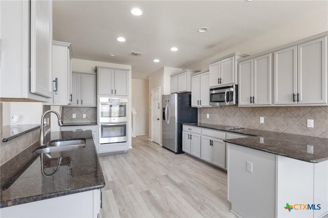 kitchen with light wood finished floors, visible vents, appliances with stainless steel finishes, a sink, and dark stone counters