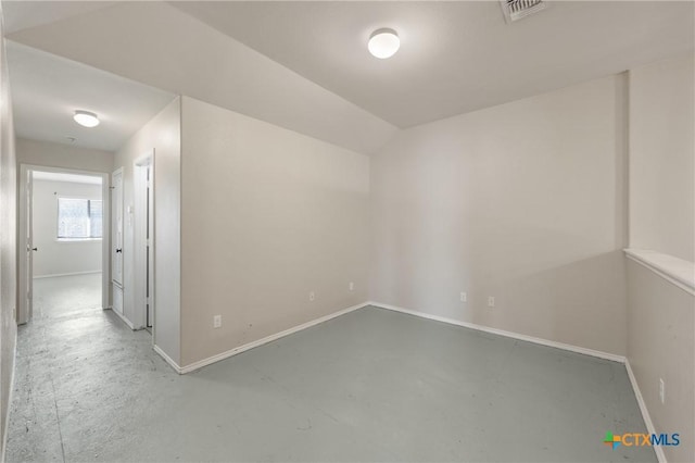 spare room featuring concrete flooring, lofted ceiling, visible vents, and baseboards