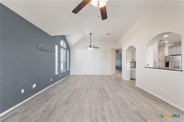 unfurnished living room with arched walkways, light wood finished floors, vaulted ceiling, ceiling fan, and baseboards