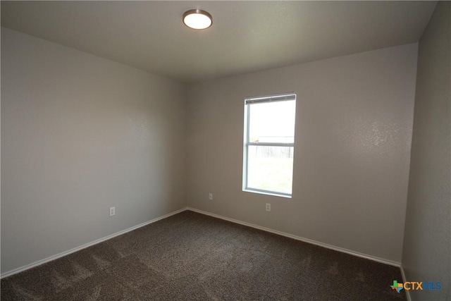 spare room featuring dark colored carpet and baseboards