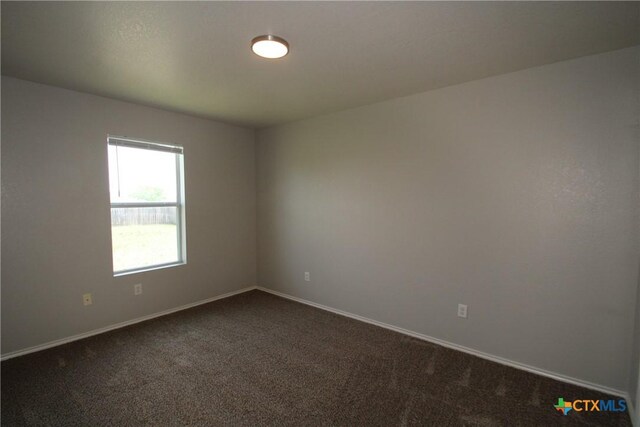 spare room featuring baseboards and dark carpet