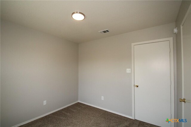 empty room featuring baseboards, visible vents, and dark carpet