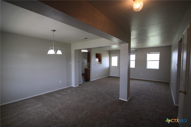 below grade area with baseboards, visible vents, dark colored carpet, and a notable chandelier