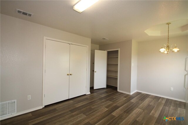 unfurnished bedroom with an inviting chandelier, baseboards, dark wood-type flooring, and visible vents