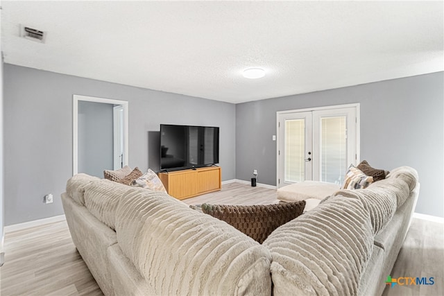 living room with french doors, light hardwood / wood-style flooring, and a textured ceiling