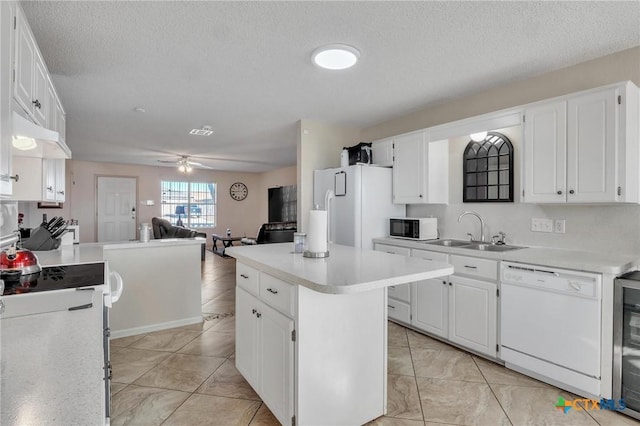 kitchen featuring white appliances, a kitchen island, ceiling fan, sink, and white cabinetry