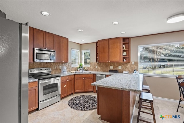 kitchen with brown cabinets, a breakfast bar area, open shelves, appliances with stainless steel finishes, and a peninsula