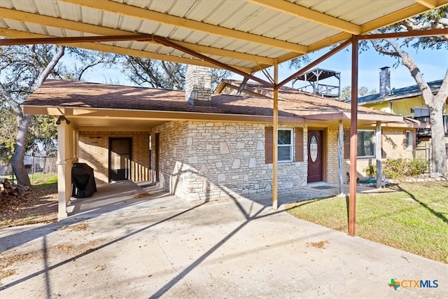 exterior space with roof with shingles, concrete driveway, an attached carport, stone siding, and a front lawn