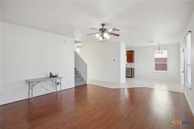 unfurnished living room featuring ceiling fan with notable chandelier and light hardwood / wood-style floors