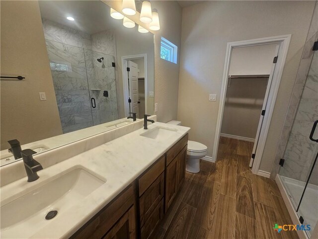 bathroom featuring double vanity, a stall shower, a sink, and wood finished floors