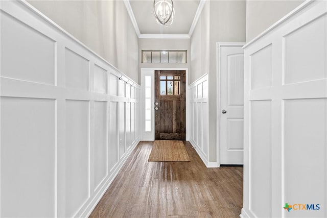 foyer with a chandelier, a decorative wall, crown molding, and wood finished floors