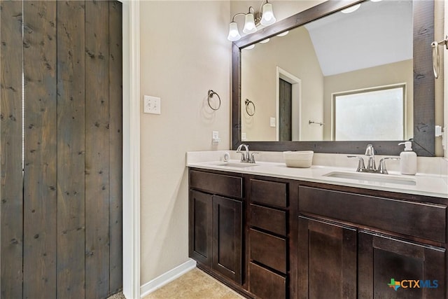 bathroom featuring a sink, baseboards, double vanity, and vaulted ceiling