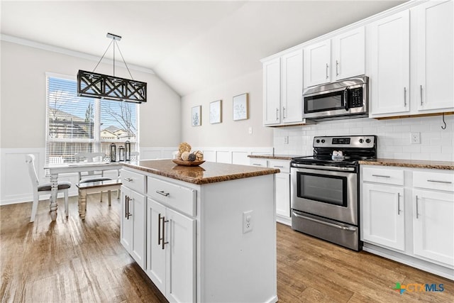 kitchen featuring wood finished floors, a wainscoted wall, appliances with stainless steel finishes, and a center island