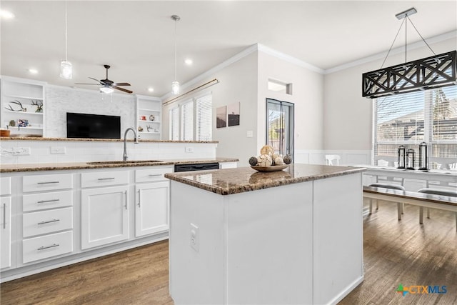 kitchen featuring dark stone countertops, a wainscoted wall, a kitchen island, a sink, and crown molding