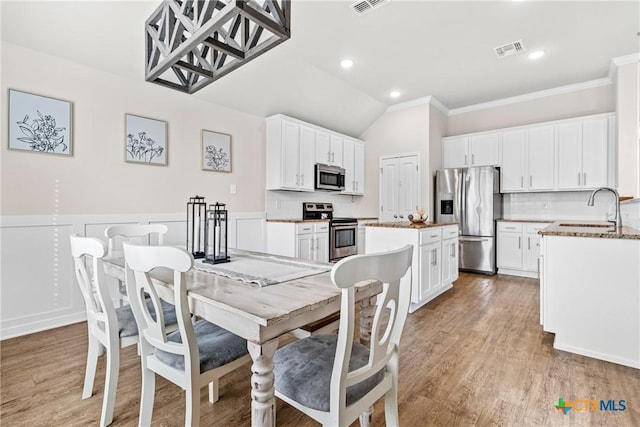 dining room featuring light wood-type flooring, visible vents, lofted ceiling, and wainscoting