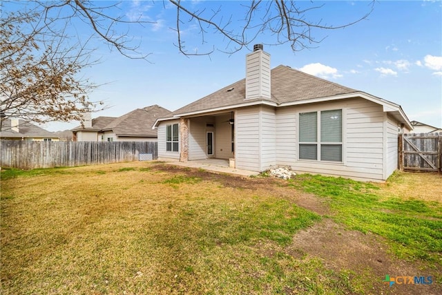 rear view of property with a lawn, a fenced backyard, a chimney, and a patio area