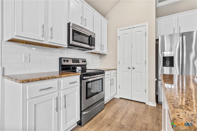 kitchen featuring backsplash, appliances with stainless steel finishes, white cabinets, light wood finished floors, and lofted ceiling