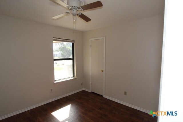 empty room featuring baseboards, ceiling fan, and dark wood-type flooring