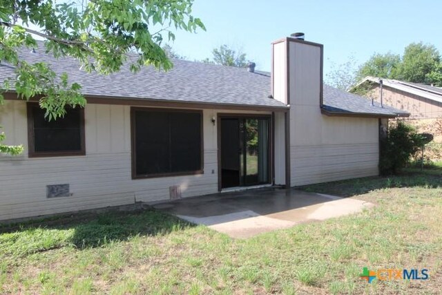 back of property with a lawn, a patio, a chimney, and a shingled roof