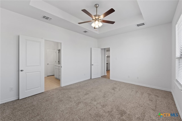 unfurnished bedroom featuring light carpet, ensuite bath, a raised ceiling, and ceiling fan