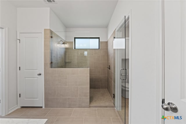 bathroom with toilet, tile patterned flooring, and tiled shower