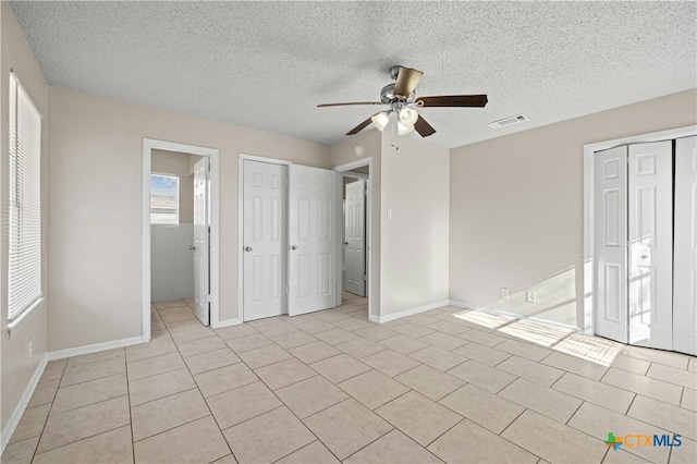 unfurnished bedroom featuring ensuite bathroom, a textured ceiling, ceiling fan, and light tile patterned floors