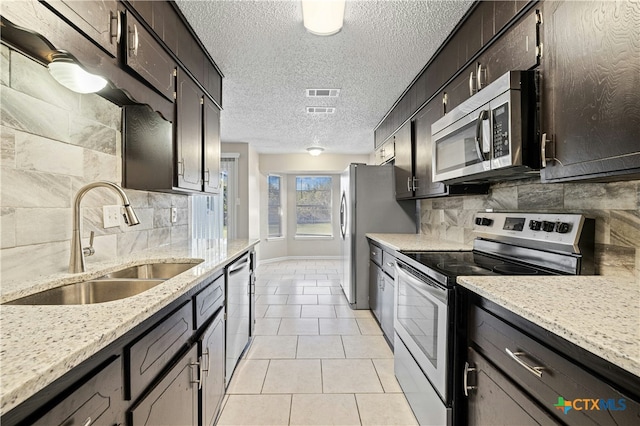 kitchen featuring a textured ceiling, stainless steel appliances, tasteful backsplash, light tile patterned flooring, and sink