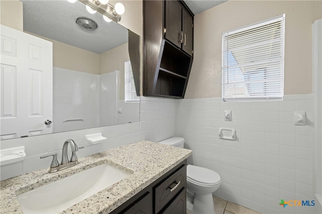 bathroom with toilet, a textured ceiling, tile walls, tile patterned floors, and vanity