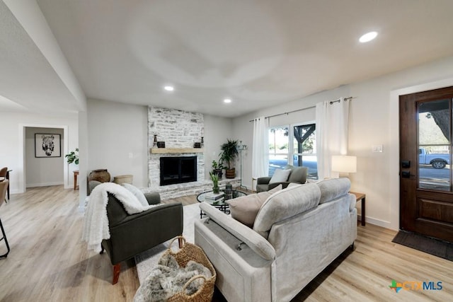 living room featuring a stone fireplace, light hardwood / wood-style flooring, and a healthy amount of sunlight