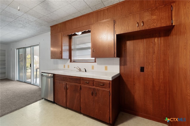 kitchen featuring tile counters, sink, stainless steel dishwasher, and wooden walls