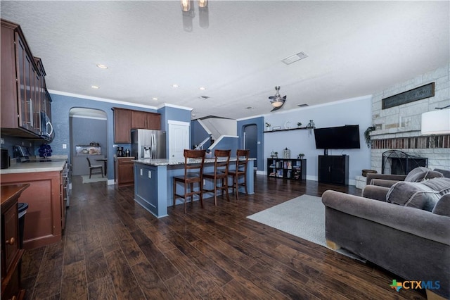 living room with arched walkways, a fireplace, visible vents, dark wood finished floors, and crown molding