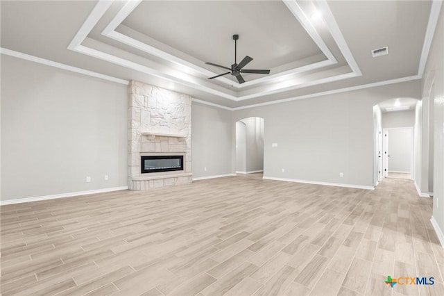 unfurnished living room featuring ceiling fan, a tray ceiling, a stone fireplace, and light hardwood / wood-style flooring