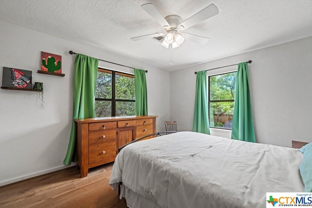 bedroom featuring a textured ceiling, light hardwood / wood-style floors, multiple windows, and ceiling fan