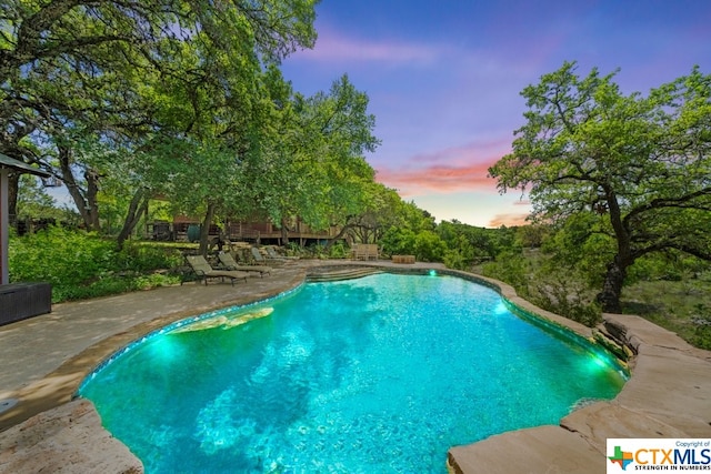 pool at dusk featuring a patio