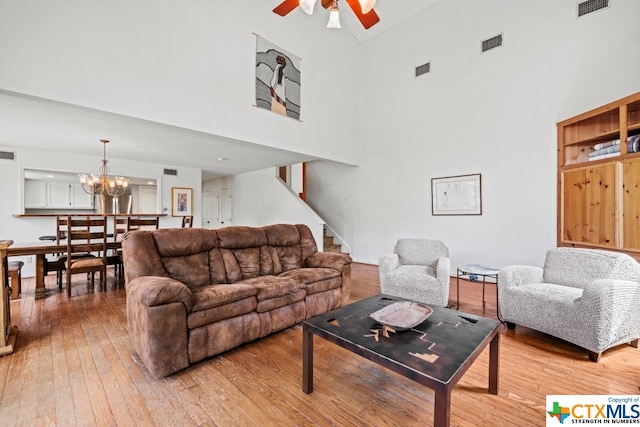 living room with a towering ceiling, ceiling fan with notable chandelier, and wood-type flooring