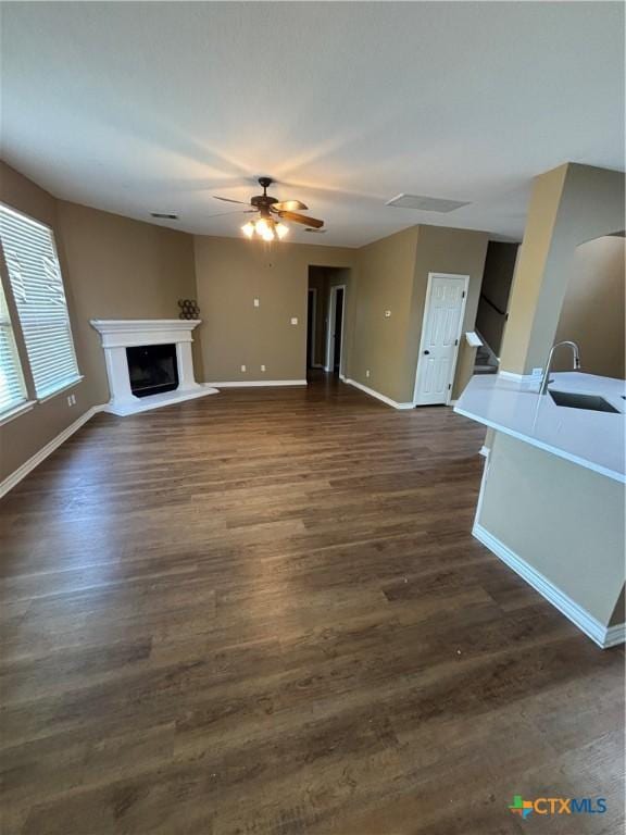322 Lone Star Blvd, Hutto, TX 78634 - unfurnished living room featuring a sink, ceiling fan, baseboards, dark wood-style flooring, and a fireplace with raised hearth