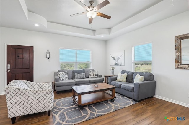 living room with a raised ceiling, ceiling fan, dark hardwood / wood-style floors, and plenty of natural light