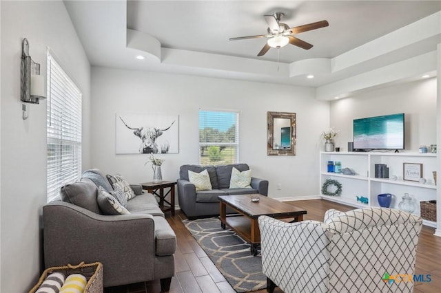 living room featuring ceiling fan, a tray ceiling, and dark hardwood / wood-style flooring